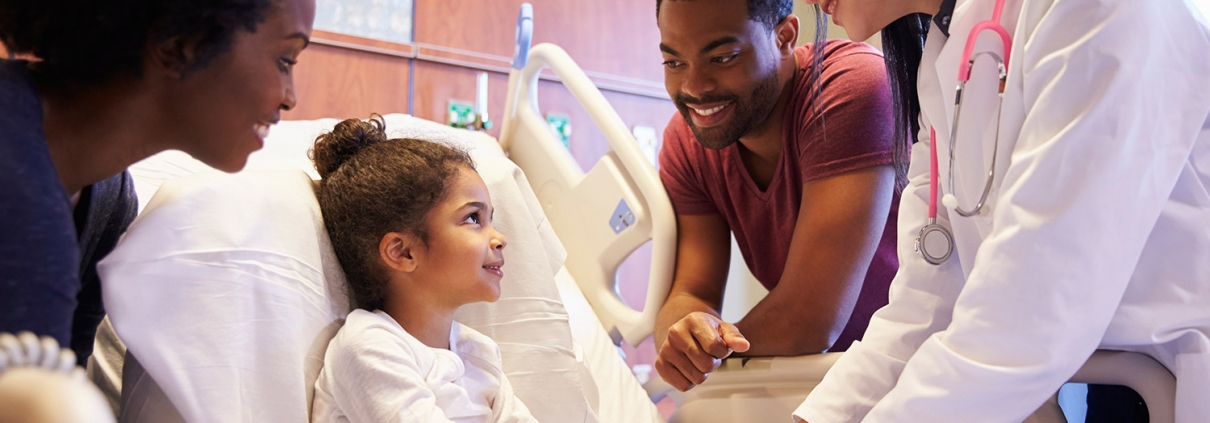 young girl in hospital bed surrounded by caring staff and family