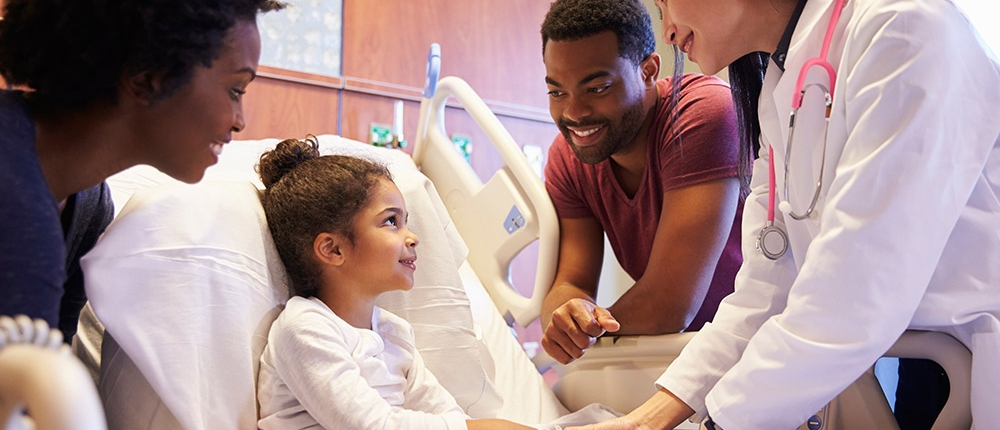 young girl in hospital bed surrounded by caring staff and family