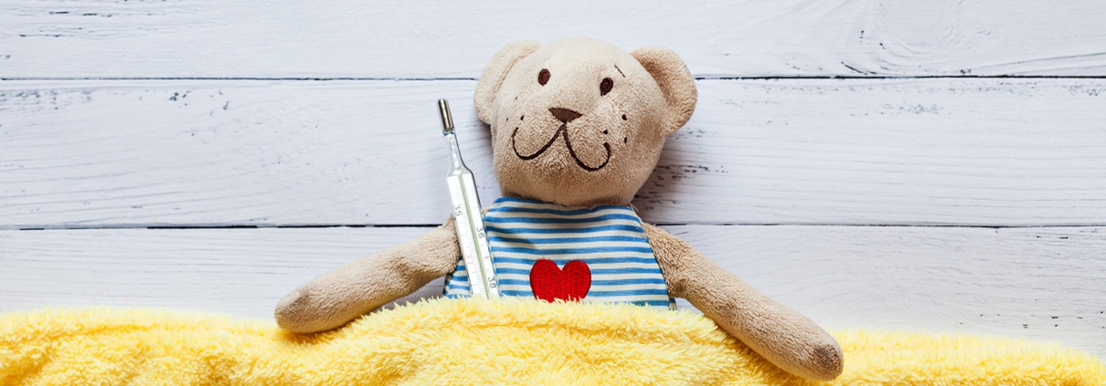 teddy beat tucked into yellow blanket and holding a thermometer